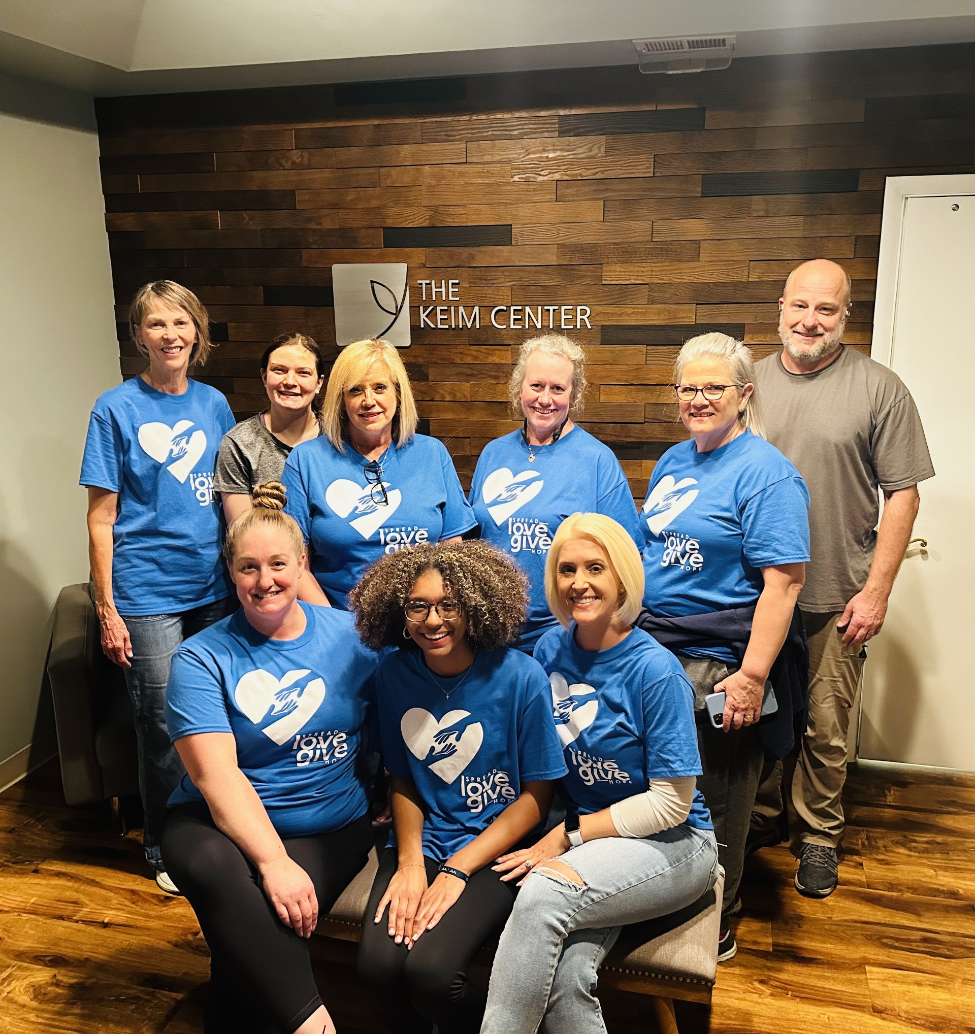 Coastal Community Church group in front of Keim Center sign. Group of women in blue shirts and one man in grey shirt