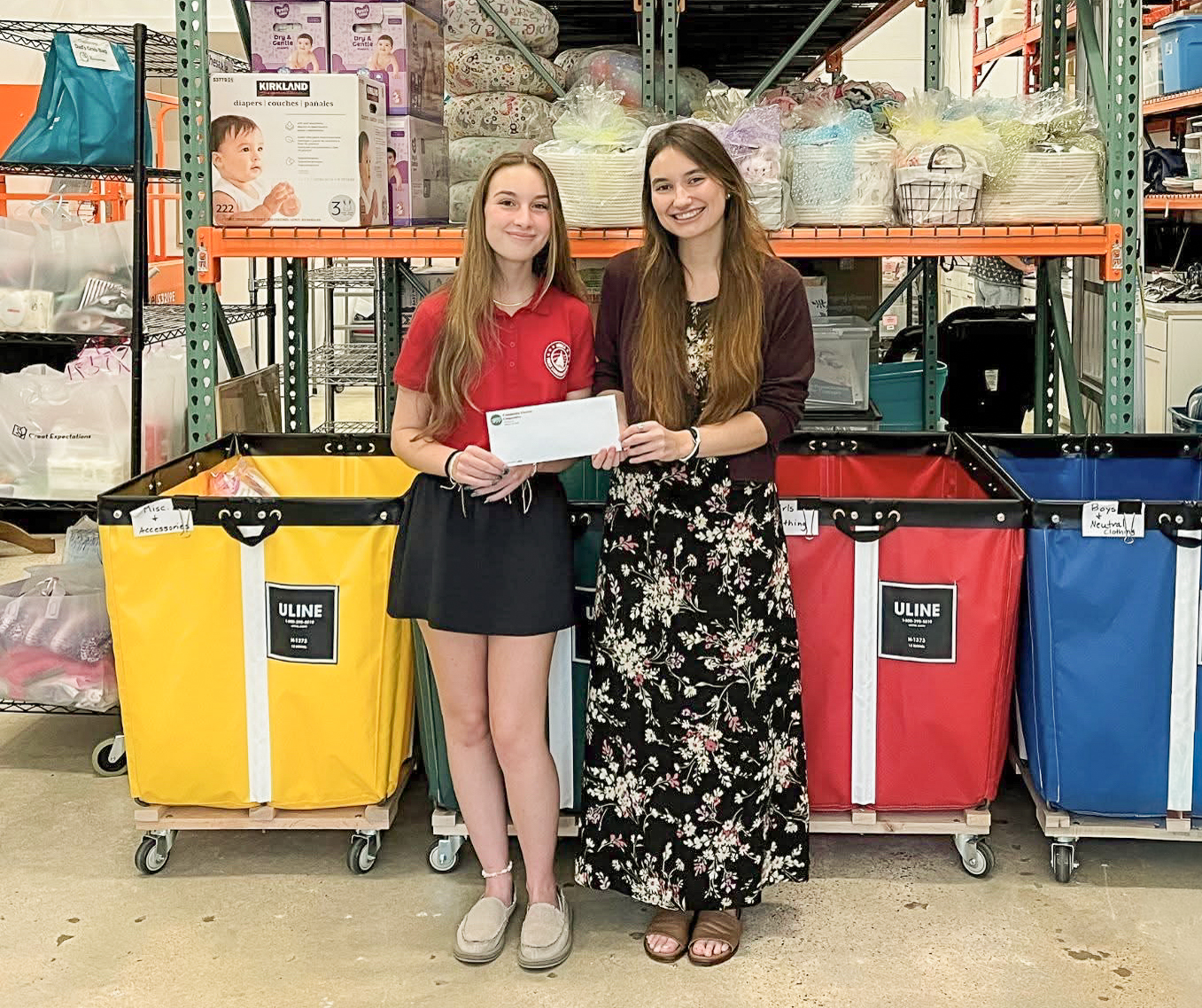 Two women in front of three multicolored bins and baby diapers.