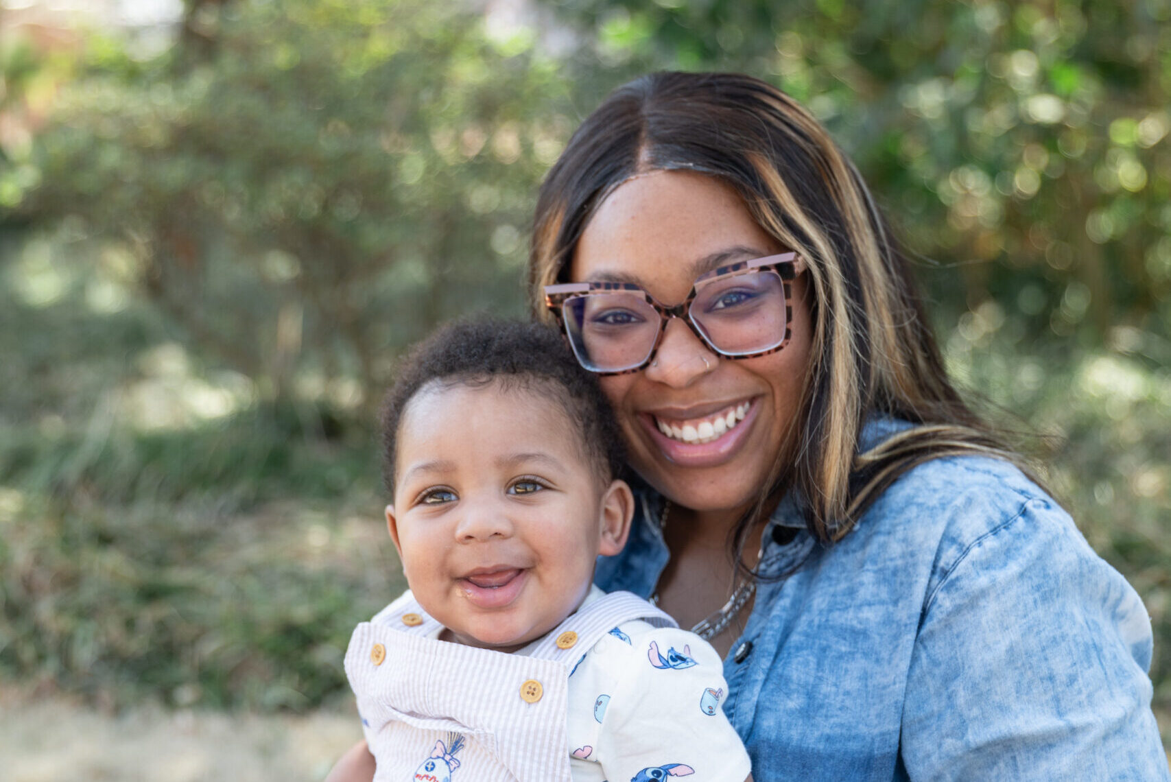 A mom dressed in blue holding her baby smiling